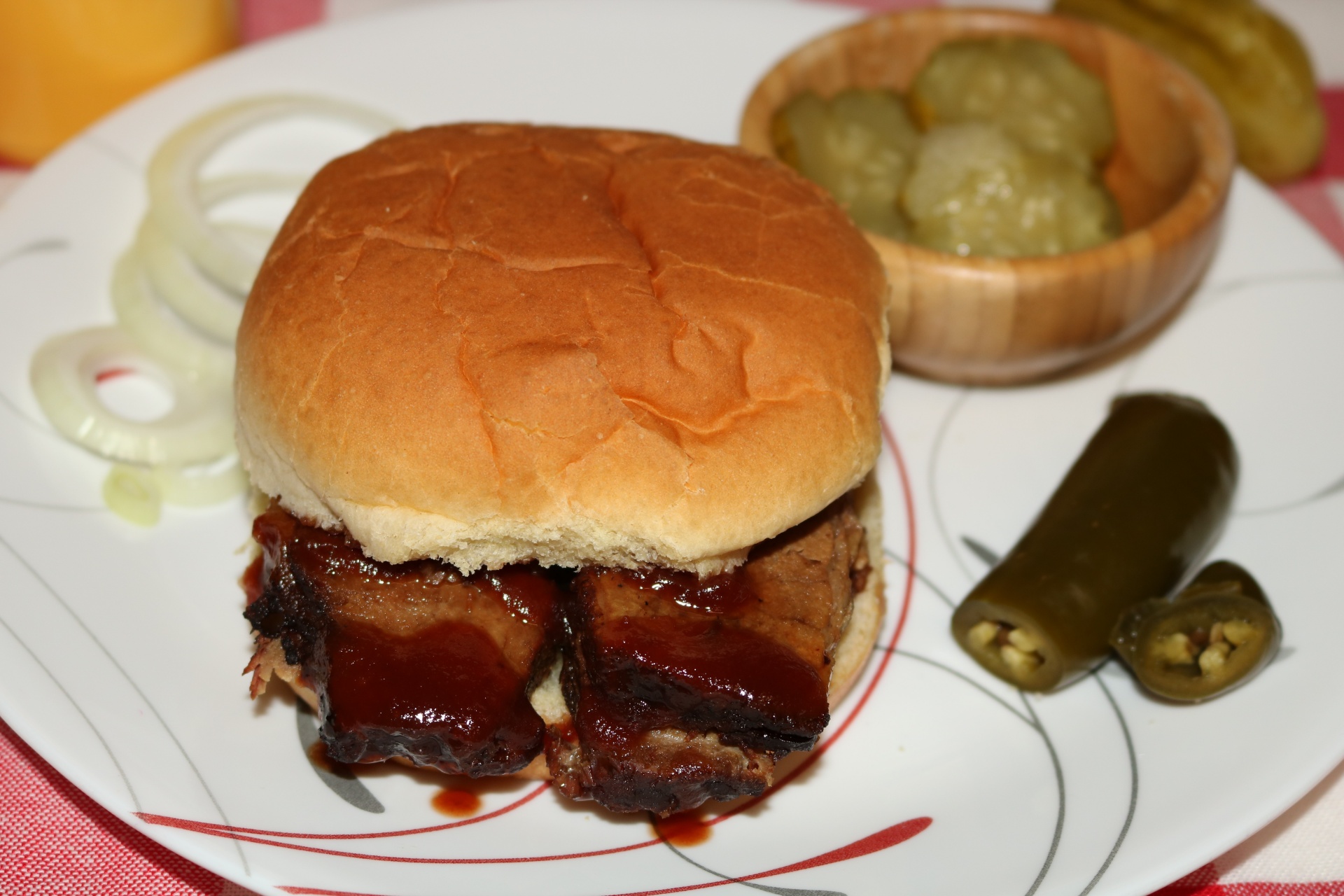 Sliced brisket barbeque sandwich on a white plate with onion, pickle and jalapeno pepper.