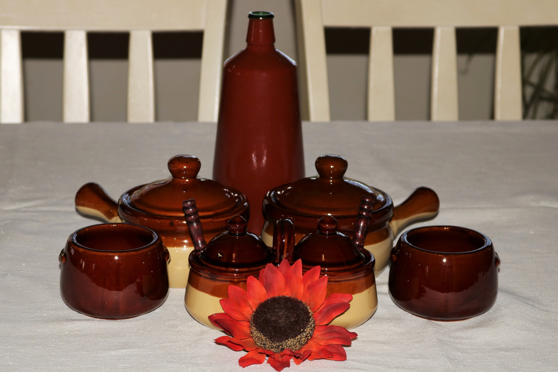 Brown glazed vintage stone ware bowls, bean pots and condiment servers, on a white table with vintage wine bottle.