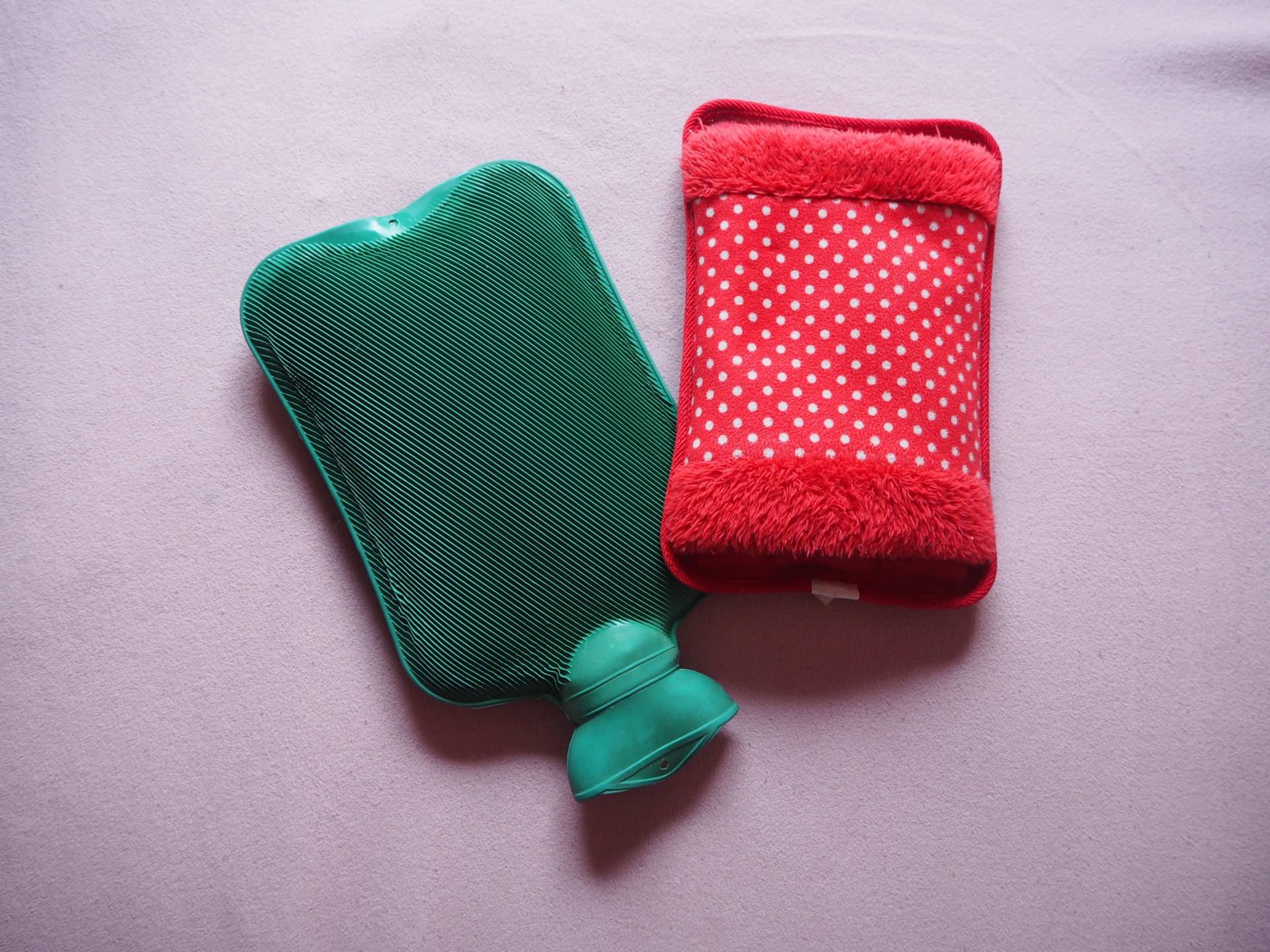 Two hot-water bags, one normal, one electric, lying on a light pink sheet