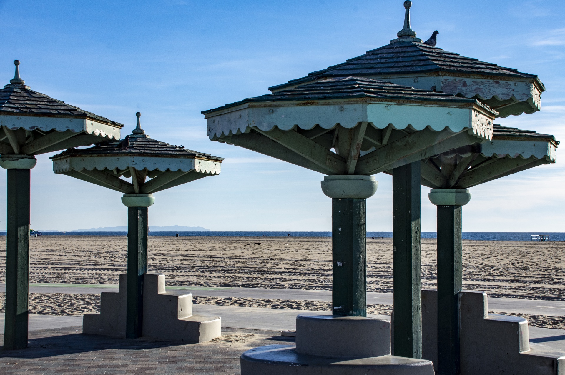 several wood canopies on shores of Venice Beach, california. One has a pigeon sitting on its roof