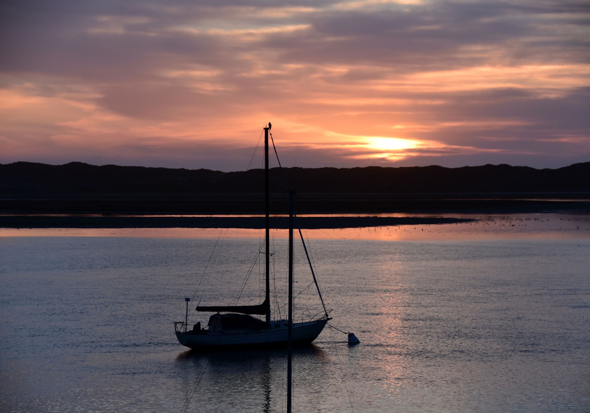 a sailboat is silhouetted against the setting sun in Morro Bay, California