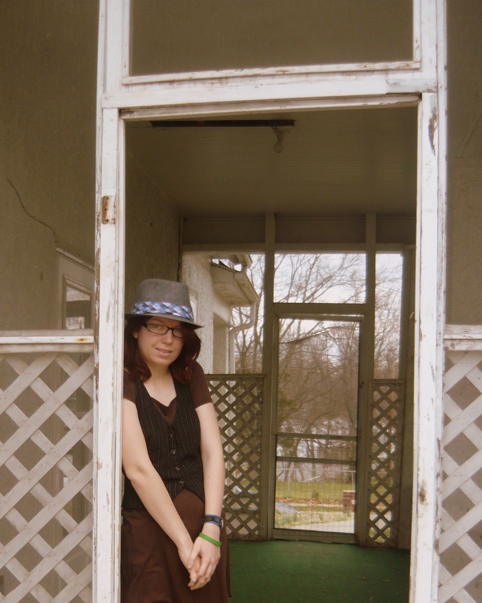 A redhead girl standing in a doorway, wearing hat and glasses