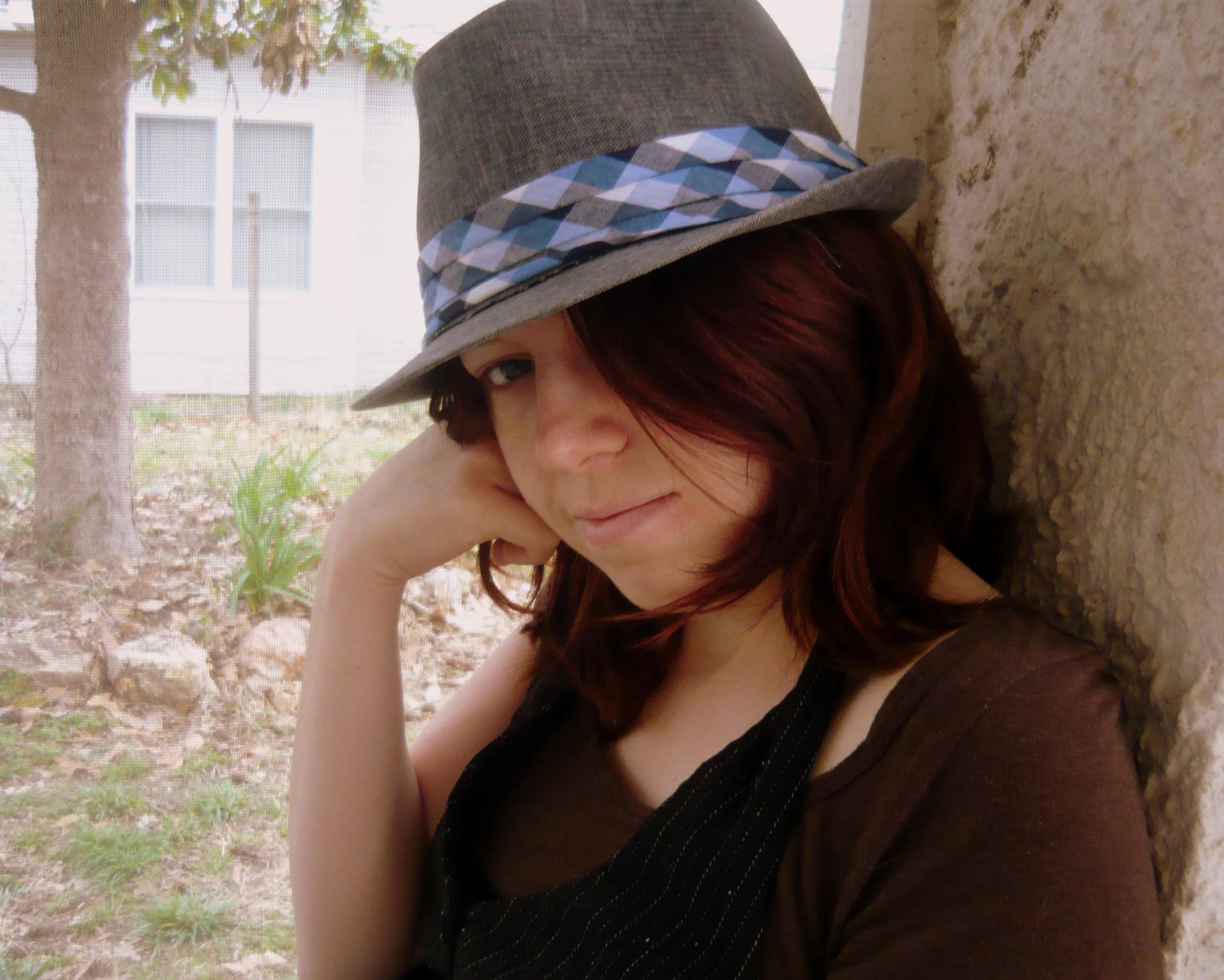 A pretty girl with red hair wears a fedora.