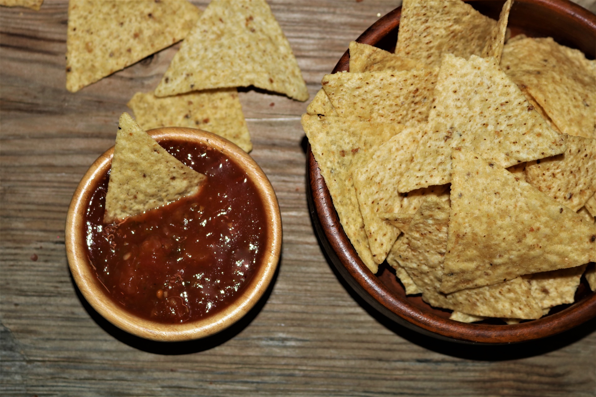 Top view of a bowl of picante sauce and a bowl of tortilla chips on a wood table.