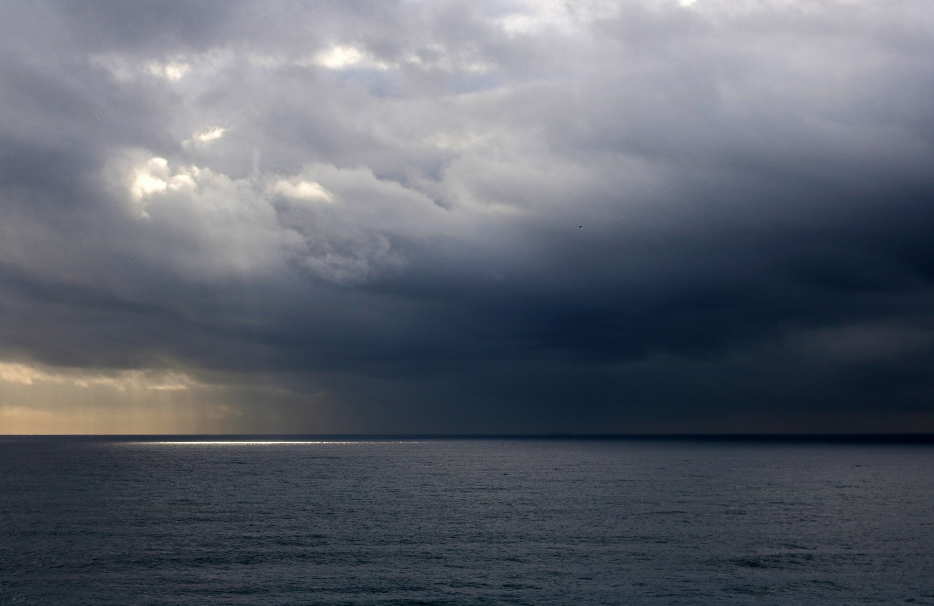 a thin sliver of light reflecting on the ocean through heavy cloud