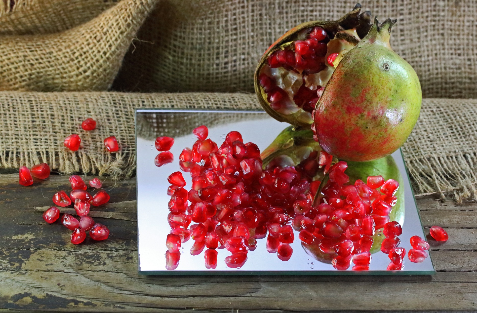 open pomegranate fruit with seeds on a mirror and wooden board