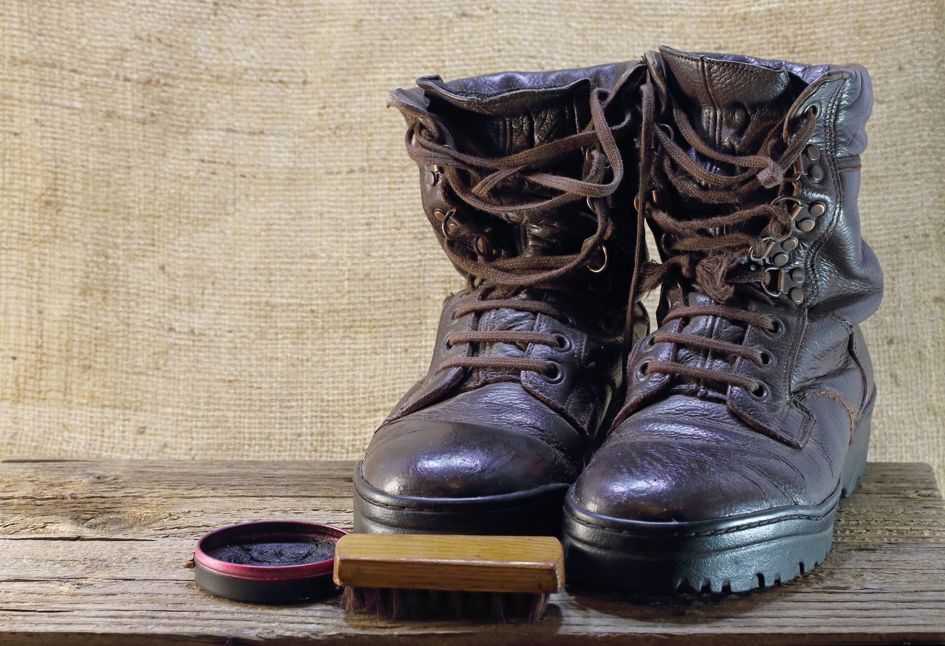 pair of old shiny combat boots with polish and brush against hessian backdrop
