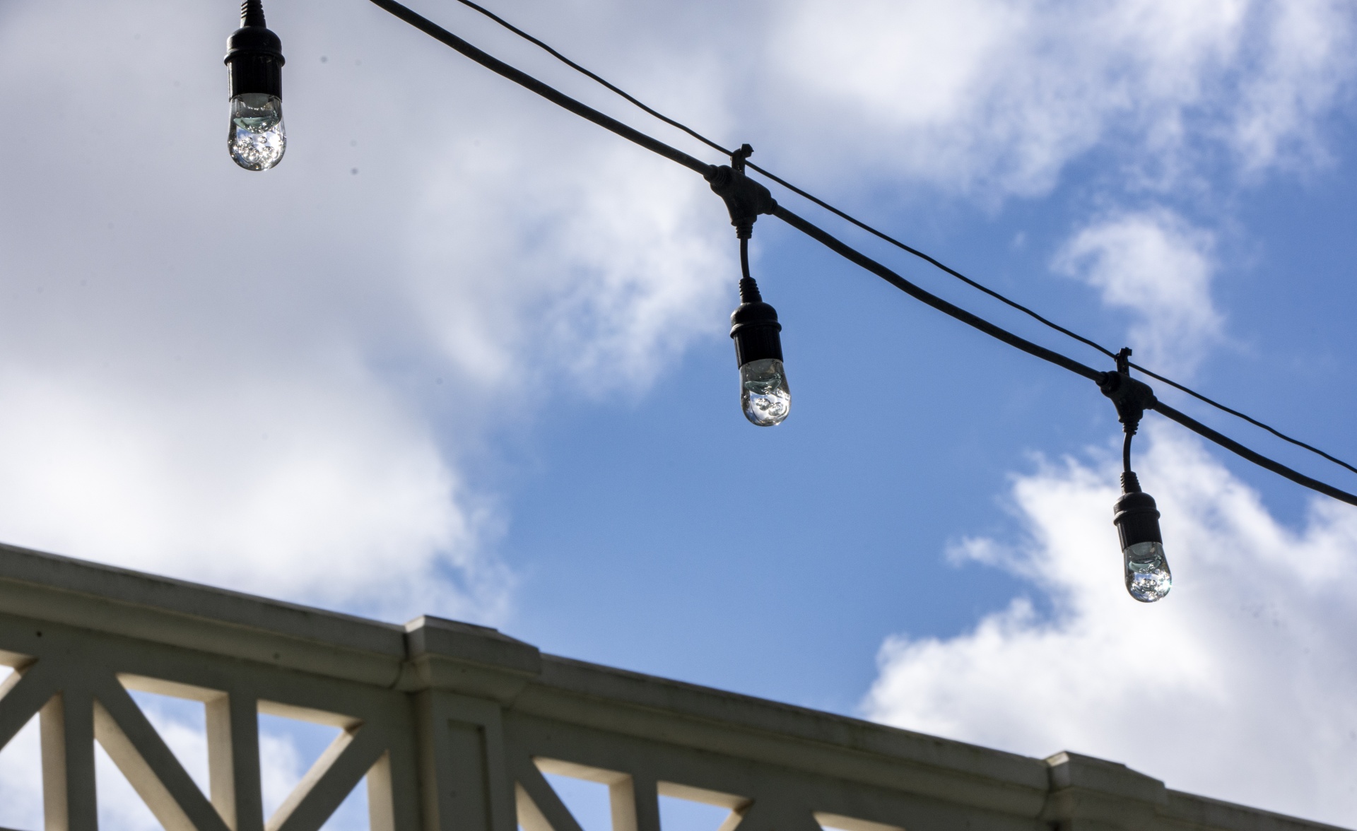 string of patio lights against a bright blue sky with white puffy clouds