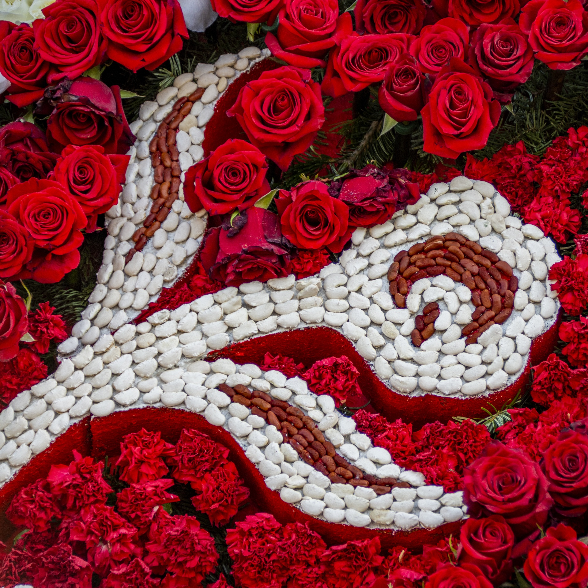 red roses and carnations surround a flower design created with beans