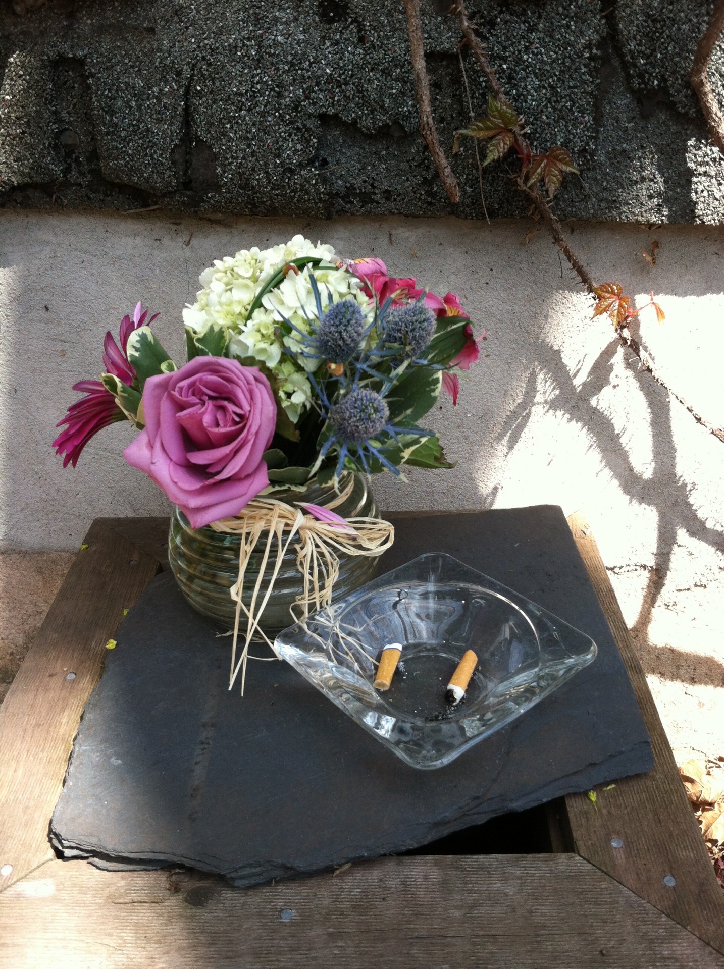 A small vase of pretty flowers sit by an ashtray holding some cigarette butts