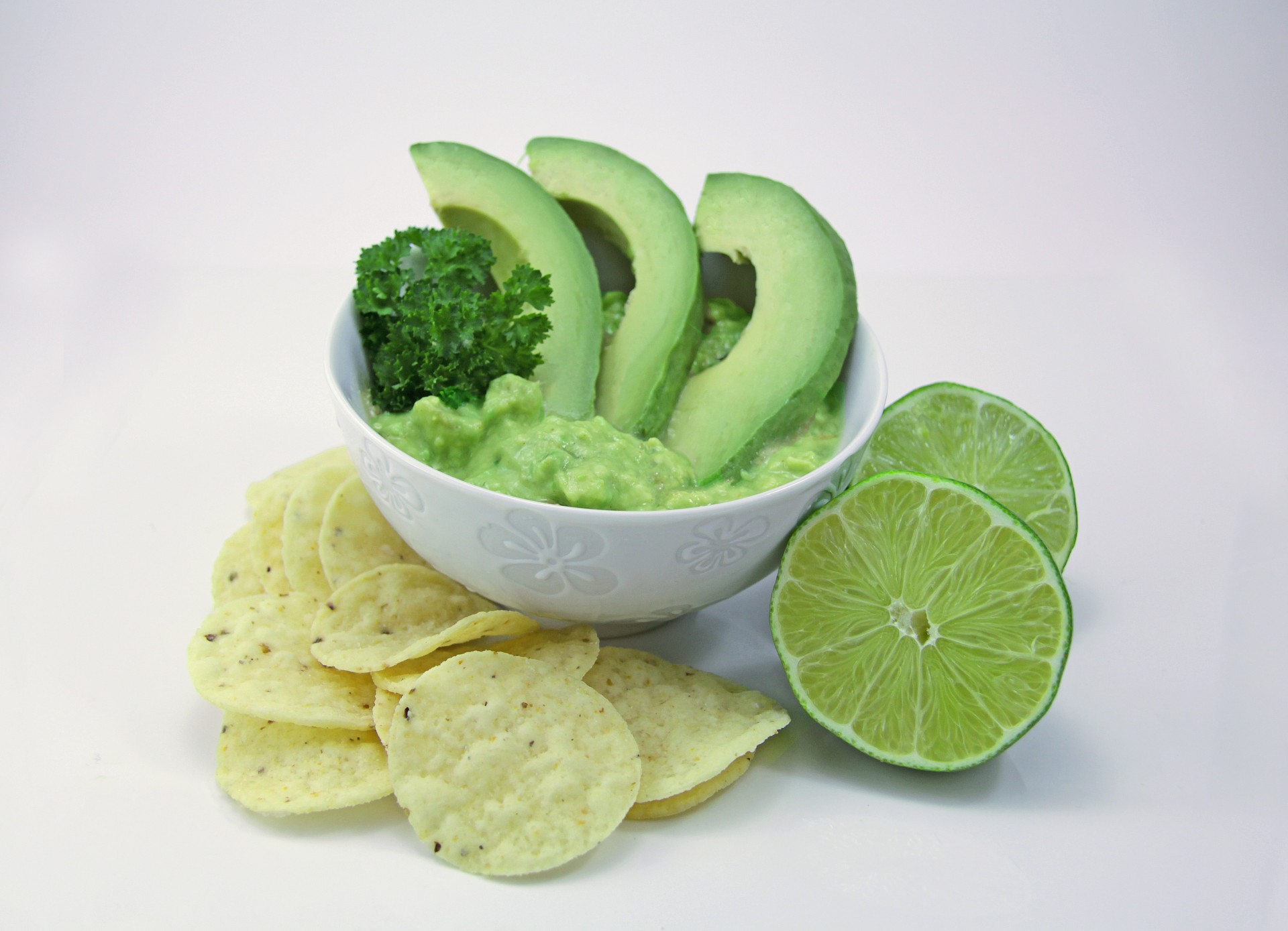 guacamole in White bowl with avocados and lime and chips on seamless white background