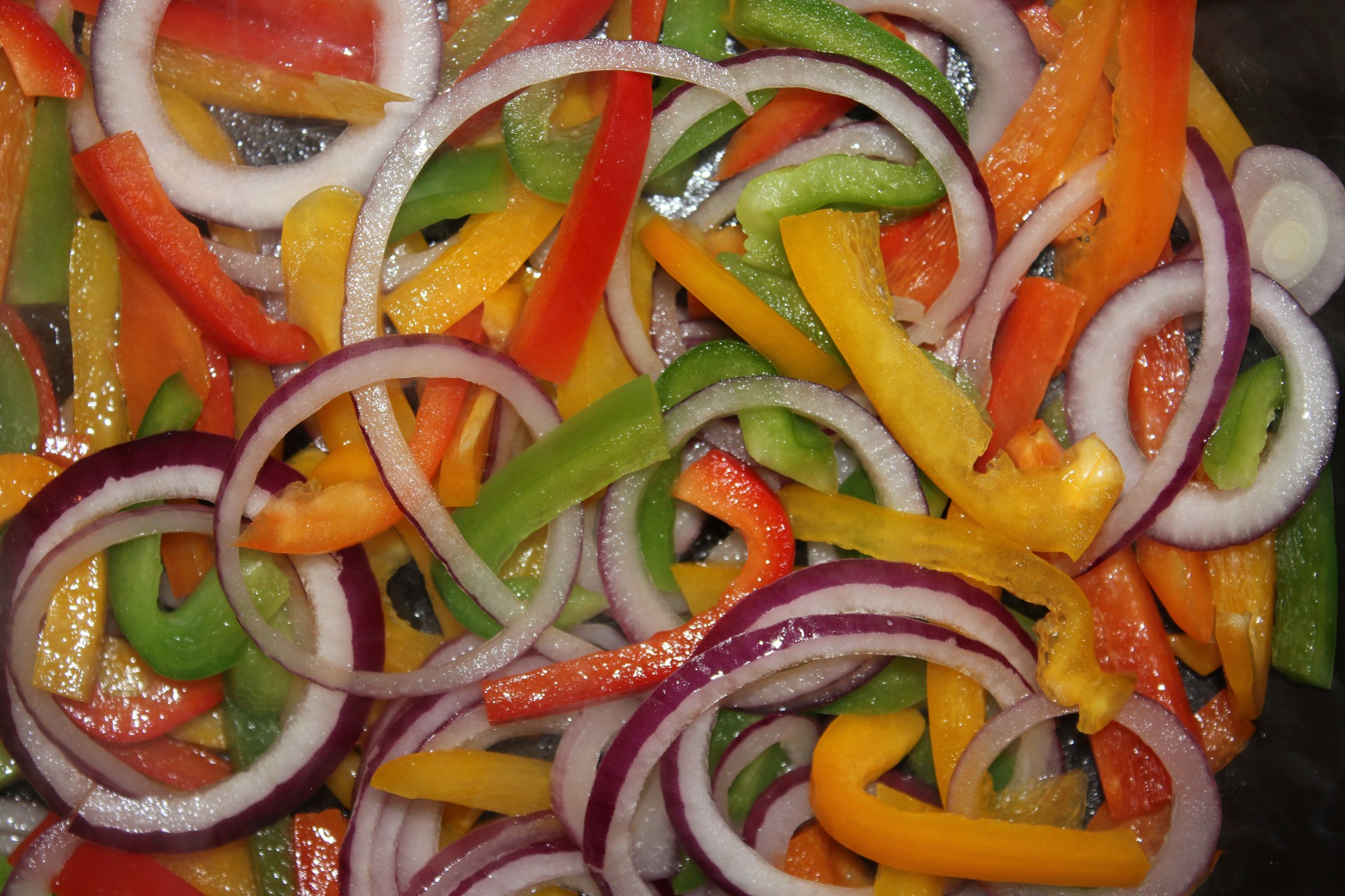 Red green and yellow paprika with red onion in frying pan.