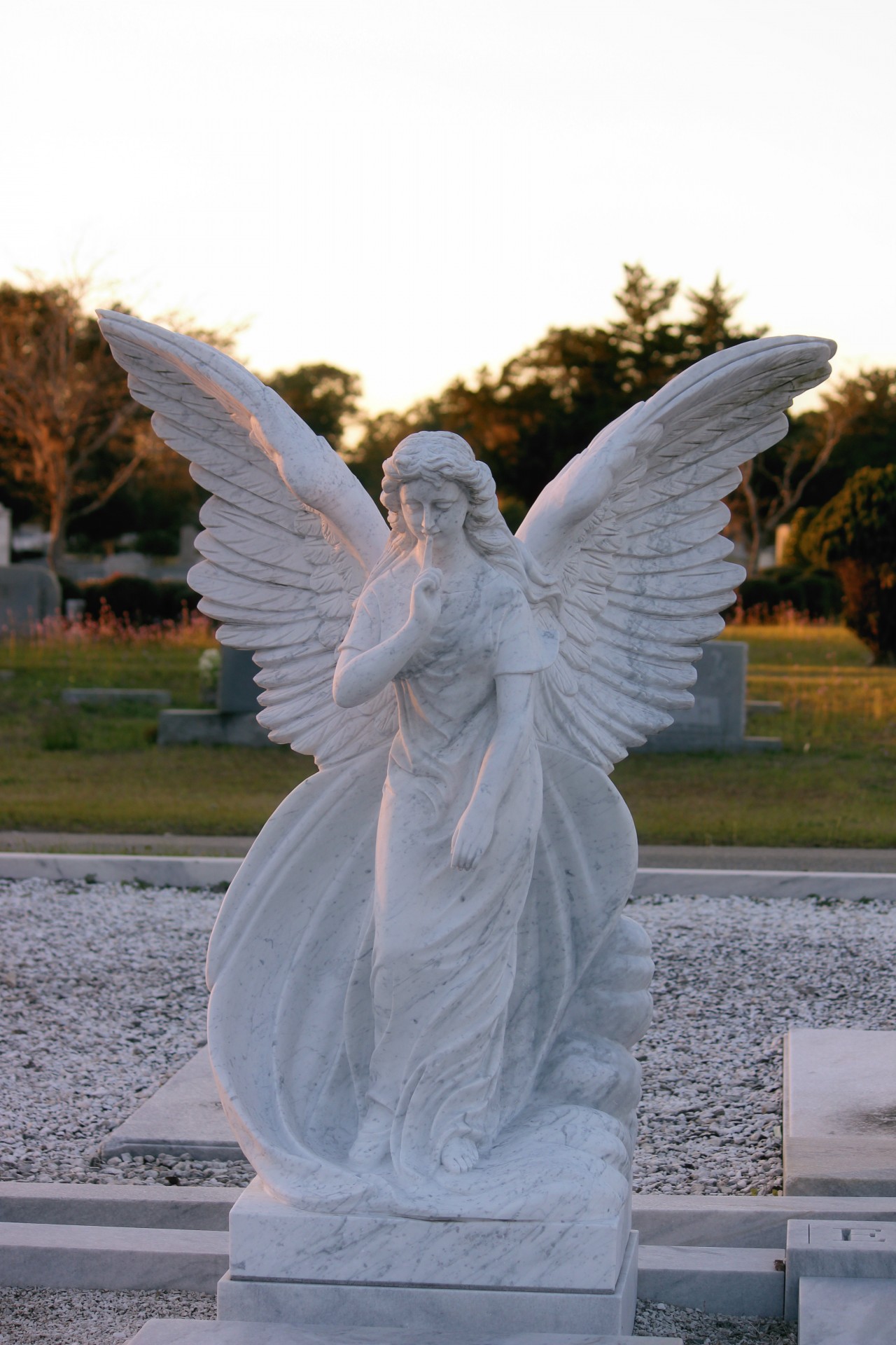 A angel statue with large wings at a cemetery watching over the graves.