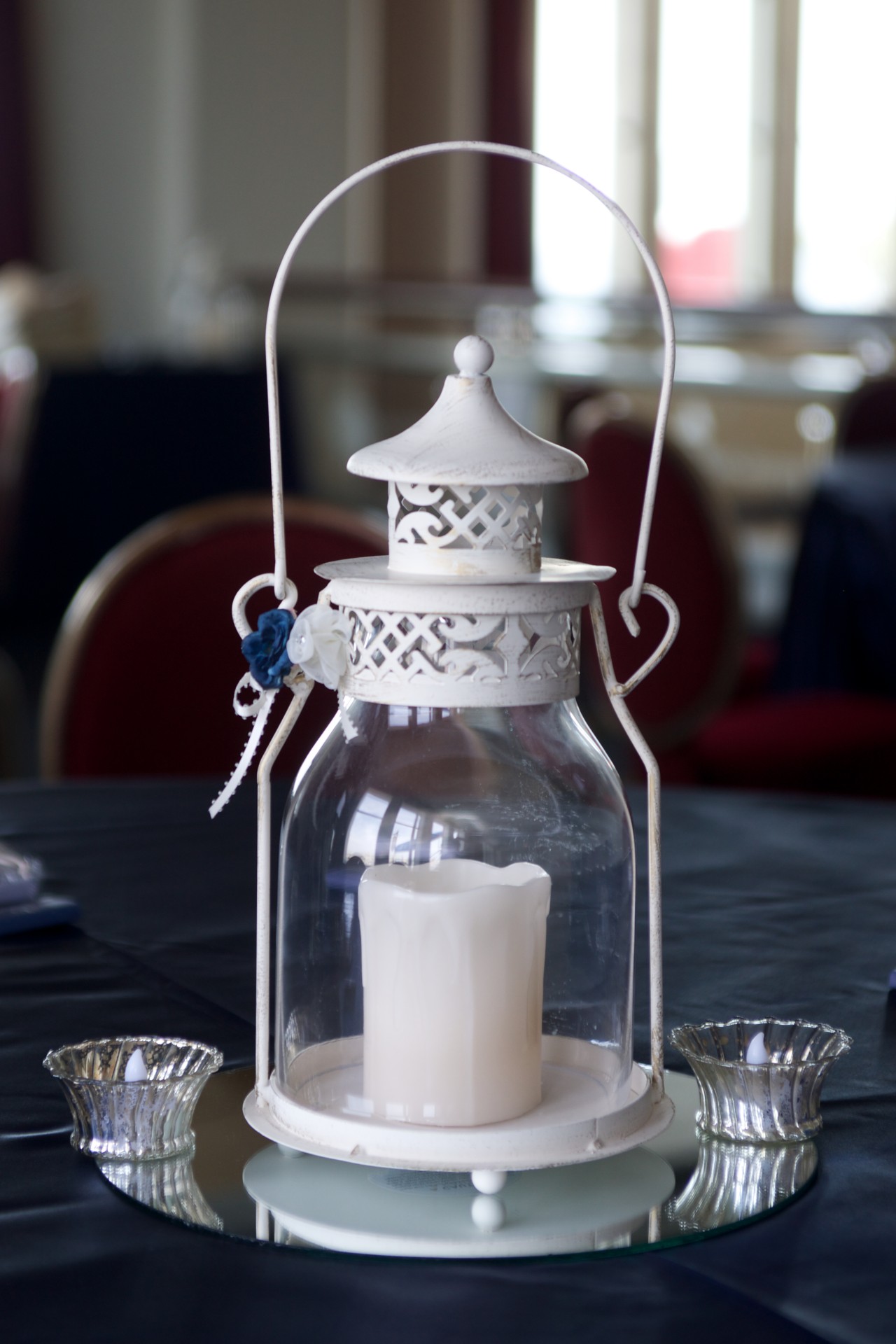 White wedding decorations of lantern and candles on a dark blue table cloth.